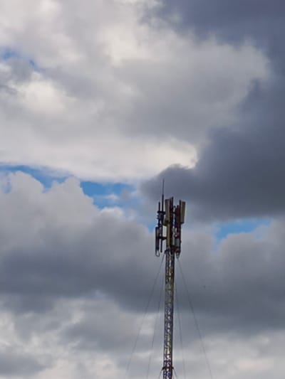 This media file shows a telecommunications tower against a dramatic sky filled with clouds. The tower, which is the primary object, is a tall, lattice-style structure with various antennas and equipment mounted on it. It appears to be a cell tower. The sky is a mix of dark gray and lighter, fluffy clouds, with patches of blue visible between them, suggesting a dynamic weather pattern, possibly approaching storm or clearing skies. The overall impression is one of a somewhat overcast or moody day. There are no people visible in the frame, and no text is discernable on the tower or in the sky. The scene is set outdoors, likely in a rural or semi-rural location where such towers are common. The image does not provide specific clues about the exact time of day, but the lighting suggests it could be daytime, perhaps late afternoon given the cloud cover and the way the light interacts with it. The location context provided indicates Biaroza, Belarus.