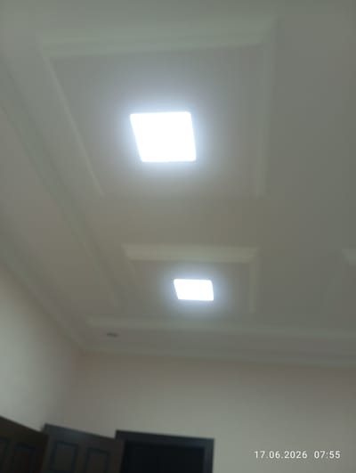 The image captures a view of a ceiling in a room. Two square, recessed lights are visible, one in the upper half of the frame and another slightly lower and to the right. The ceiling has a layered, stepped design with ornate trim. In the bottom left corner, the tops of dark wooden cabinets or doors are visible, suggesting furniture or architectural features below the ceiling. The timestamp "17.06.2026 07:55" is overlaid on the bottom right of the image. The scene appears to be indoors, likely a residential or office space. The location is specified as Ohangaron, Uzbekistan.
