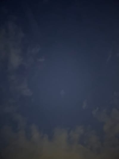 This media file captures a night sky with visible clouds and a few faint stars. The overall color palette is dominated by deep blues and grays, suggesting it was taken after dusk or before dawn. The clouds are wispy and scattered, with some illuminated by an unseen light source, possibly artificial light from the ground or moonlight. The scene appears to be an outdoor setting, likely in a relatively dark area to allow for the visibility of stars. There are no people or specific objects in the frame, focusing solely on the atmospheric conditions of the night sky. The location context provided is Змейка, Russia. There is no visible text in the image.