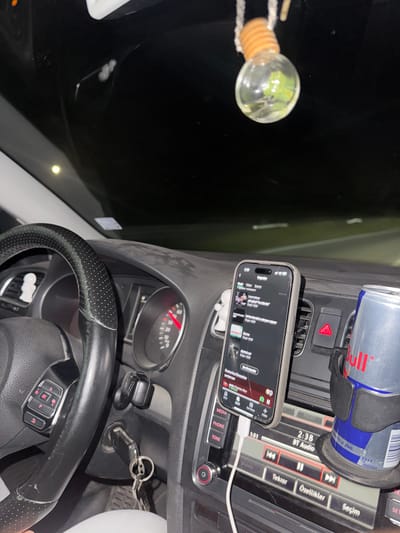 The image depicts the interior of a car at night. The driver's perspective shows the steering wheel on the left, dashboard instruments including a speedometer with a red needle indicating speed, and the central console with a smartphone mounted in a holder. The phone screen displays a music app with a playlist. A Red Bull can is also visible in a cup holder. Outside the car, the darkness suggests a rural or highway setting. The presence of the car and its occupants implies they are in transit. The scene is likely a private vehicle, and the time of day is night. The location is specified as Stanyantsi, Bulgaria.