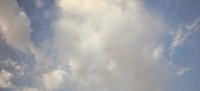 The image is a close-up shot of a cloudy sky with a clear blue sky visible in the background. The clouds are a mixture of white and gray, with some areas appearing brighter due to sunlight. The image was taken in Margilan City, Uzbekistan. There are no people, subjects, objects, or actions depicted in the image. The environment is solely the sky.