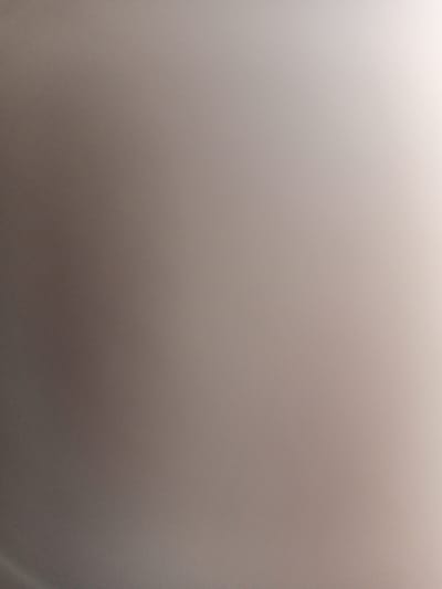 The image is an abstract, out-of-focus photograph with a gradient of color from dark grey on the left to a bright white on the right. There are no discernible objects, people, or actions. The lighting appears to be coming from the upper right corner, creating a bright highlight in that area. The background is a uniform, textured surface with visible grain. There is no indication of the city of Romodan, Ukraine, or any specific environmental details that could be used for forensic analysis.