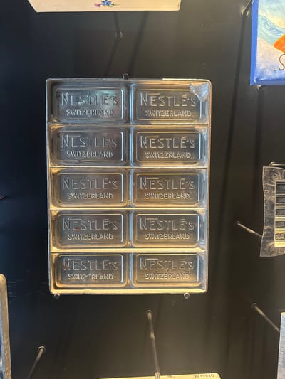 The image shows a metal mold for making Nestle's chocolate bars. Each of the ten rectangular cavities is embossed with "NESTLE'S" and "SWITZERLAND". The mold is presumably on display in a location associated with Nestle's history, possibly at the Nestle headquarters in Kilchberg (ZH), Switzerland.