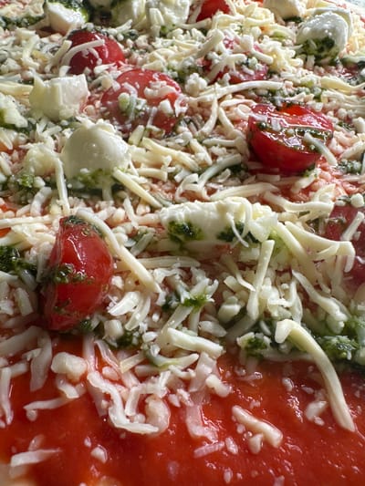 The image shows a close-up, overhead view of a raw pizza topped with tomato sauce, shredded cheese, cherry tomatoes, and mozzarella balls. The pizza is not in Sankt Wendel, Germany; it is a food item. There are no people or any environmental details visible.
