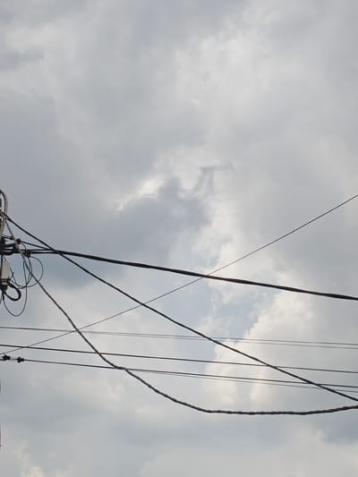 The image shows a view of a cloudy sky with overhead power lines. The power lines are strung across the frame, some taut and others with a slight sag. A cluster of wires and equipment is visible on the left side of the image, suggesting a utility pole or connection point. The clouds are varied in density, with some appearing thicker and darker than others, hinting at a potentially overcast or stormy day. The overall impression is one of urban infrastructure set against a natural sky. No people are visible in the image. The specific location in Koledino, Russia, is not visually discernible from the image itself, but the presence of overhead power lines is typical of many populated areas.
