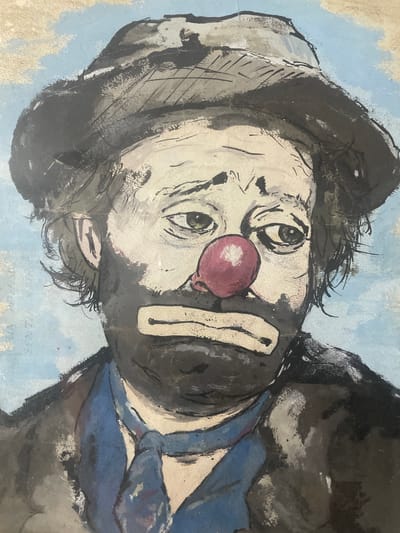 The image is a close-up watercolor painting of a sad clown's face. The clown is wearing a dark hat and a blue tie. The clown's face is painted with dark makeup around the eyes and mouth, and a red nose. The background is a pale blue with some wispy white clouds. The painting style is expressive, with visible brushstrokes and a somewhat rough texture. The image does not depict any specific location in Santa Marta, Colombia.