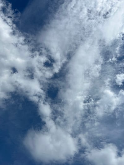 The image depicts a sky filled with a mix of white, fluffy clouds and darker, wispy formations against a deep blue backdrop. The clouds appear to be scattered and varied in density, with some areas of clear blue sky visible between them. The lighting suggests it is daytime, possibly with the sun partially obscured by the clouds. There are no visible structures, people, or specific geographical landmarks to indicate a precise location within Парыцкі сельскі Савет, Belarus. The scene is solely focused on the natural sky and cloudscape.