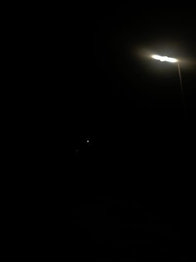 The image is extremely dark, making detailed analysis difficult. The predominant color is black, suggesting a nighttime or low-light environment. In the upper-left corner, there is a bright, elongated light source that appears somewhat irregular in shape. A light streak extends horizontally from it towards the right. Two small, distinct, white spots are visible near the center of the frame. Without further information, determining the context, objects, actions, location (Wysoka, Poland), or subjects within the image is limited.