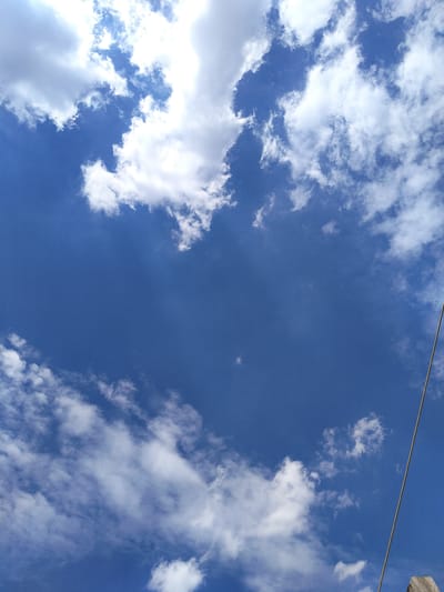 The image is a photograph of a bright blue sky with scattered white clouds. A thin, light-colored wire runs diagonally from the upper right to the lower right corner of the frame. There is a hint of a wooden post at the very bottom right edge. The scene is an outdoor environment, with no people or specific landmarks identifiable. The location in Luhansk, Ukraine cannot be determined from the visual information provided.