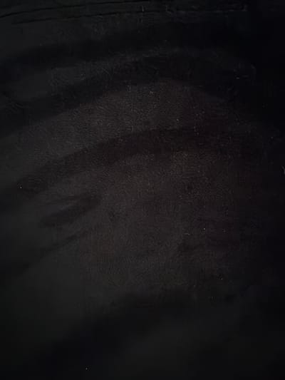 The image shows a close-up of a dark, textured surface, possibly leather or a similar material. There are variations in tone and subtle patterns of light and shadow across the surface. A seam is visible on the left side of the frame. The location in the city of Sion, Switzerland is not discernible from the image. No people, subjects, objects, actions, or interactions are identifiable within the visual information provided.