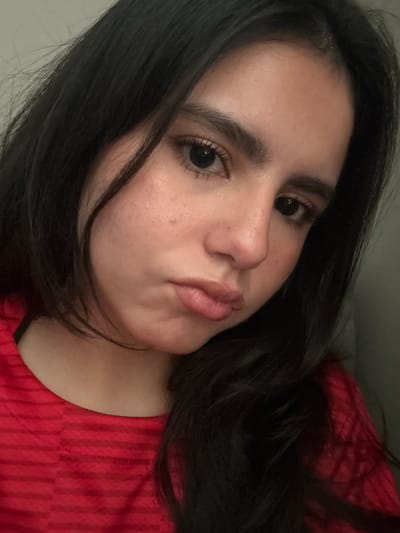 A close-up portrait depicts a woman with dark hair, brown eyes, and a fair complexion. She is wearing a red, vertically striped shirt. Her lips are slightly pursed. The background is indistinct. It is not possible to determine her location within College Station, United States of America based solely on this image.