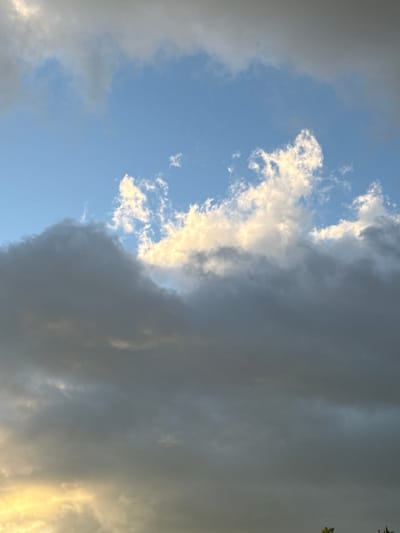 The image displays a dramatic sky over Voeikovo, Russia, featuring a stark contrast between a bright, clear blue sky and heavy, dark storm clouds. The clouds occupy the majority of the frame, with a dense, ominous mass dominating the right side of the image. To the left, the sky transitions to a lighter shade, with scattered white clouds illuminated by sunlight, suggesting a receding storm or the edge of the storm front. The lighting indicates it is either early morning or late afternoon, with the sun's rays catching the edges of the lighter clouds, creating a soft, ethereal glow. The overall impression is one of impending or just-passed weather, conveying a sense of power and natural grandeur. There are no people, objects, or discernible text within the frame. The scene is purely a natural landscape of the sky.