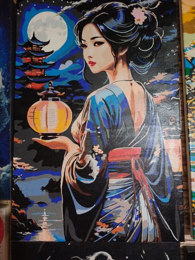 This media file is a painting of a Japanese woman at night. The woman, depicted from the back and looking over her shoulder, is wearing a blue kimono with a red obi. She is holding a lit yellow lantern in her right hand. The background features a large full moon, a pagoda, silhouetted trees, and a body of water reflecting the moonlight. The scene appears to be a serene night in a traditional Japanese setting. The painting style is reminiscent of paint-by-numbers, with distinct blocks of color. There is no visible text in the image.