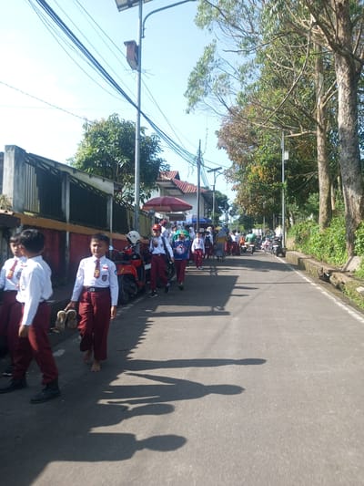 A group of children are walking along a road. They are wearing school uniforms of white shirts and maroon pants. Some children are wearing shoes while others are barefoot or carrying their shoes. There are motorbikes parked along the side of the road. There is a fence on one side of the road and trees on the other side. The image was not taken in Nhot Chang, Laos.