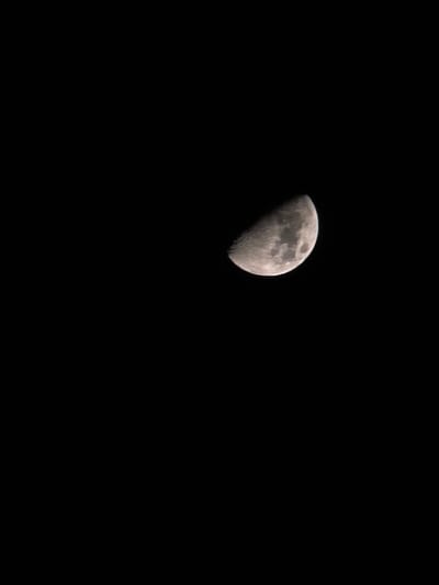 This image, captured from the city of Trachoni, Cyprus, presents a sharply detailed first-quarter or third-quarter moon set against a uniform black night sky. The moon exhibits distinct craters and darker maria across its illuminated half, with the terminator line clearly defining the boundary between light and shadow. No stars, other celestial bodies, human figures, objects, or activities are visible within the frame, which is entirely dominated by the lunar disk and the dark expanse of space.