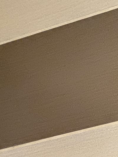 The image is an abstract, close-up shot of a textured surface. It features two distinct horizontal bands of color. The upper band is a light, sandy beige, while the lower and wider band is a darker, muted brown. The texture appears to be a woven fabric or possibly a textured paper, with subtle lines and variations visible upon close inspection. The lighting creates a slight shadow where the two bands meet, adding a subtle depth to the image. The photograph is taken from a slightly elevated angle, looking down. There are no people, animals, or identifiable objects in the frame. The background is entirely filled by this textured surface. There is no visible connection to the city of Kielce, Poland, or any other specific geographical location.