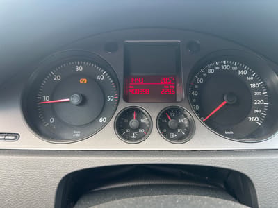 The image shows a car's dashboard, specifically the speedometer, odometer, and a digital display. The speedometer is calibrated in km/h and shows a needle pointing between 10 and 20, likely around 15 km/h. The digital display shows the time as 14:43, the outside temperature as 28.5°C, the total odometer reading as 400398 km, and the trip odometer reading as 229.5 km. There is also a small gauge showing engine temperature, with the needle pointing just above 90°C, and a fuel gauge showing slightly more than 1/1. A parking brake indicator light (orange circle with a 'P') is illuminated on the speedometer dial. The dashboard is made of dark gray textured plastic. The surrounding environment is not visible, but the image was taken inside a car. There is no indication that this image was taken in Ruzhyn, Ukraine.