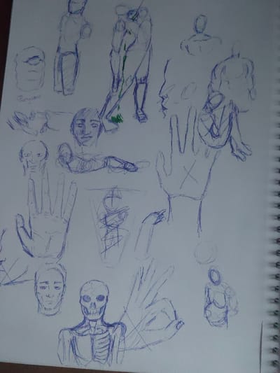 The image shows a page from a sketchbook filled with various drawings done in blue ink. The drawings include several human figures, some in profile, some in full view, and some partially obscured. Several hands are drawn, as well as a skull and rib cage. The drawings are not fully formed and appear to be practice sketches. The image is likely from a sketchbook in Yoksolovo, Russia, as the provided coordinates place the location in the city. The background is white, with a spiral bound notebook edge visible on the right side of the image. The image appears to be a candid snapshot of an artist's work.