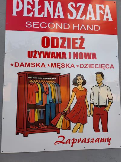 A large, rectangular, white sign with red lettering and graphics is displayed outdoors, mounted on a grey wall. The sign advertises a clothing store. The topmost text in large, white, serif font reads "PEŁNA SZAF A", which translates to "FULL CLOSET". Below this, in smaller white serif font, is "SECOND HAND".

The middle section of the sign features large, bold, red text: "ODZIEŻ", meaning "CLOTHING". Beneath this, in smaller red text, it says "UŻYWANA I NOWA", meaning "USED AND NEW".

To the left, an illustration depicts an open, dark red wardrobe filled with colorful clothing hanging on a rack. Below the hanging clothes, a pair of red shoes and orange high heels are visible. To the right of the wardrobe, an illustration of a man and a woman are shown. The woman wears an orange dress and holds two shopping bags. The man wears a white button-down shirt and red pants.

At the bottom of the sign, in red script font, is the word "Zapraszamy", meaning "We invite you". The sign is secured to the wall with visible screws. The image is cropped such that the bottom edge of the sign rests on a grey surface, likely a sidewalk or ground. The context of Stryków, Poland, is provided as the location where this sign is found.