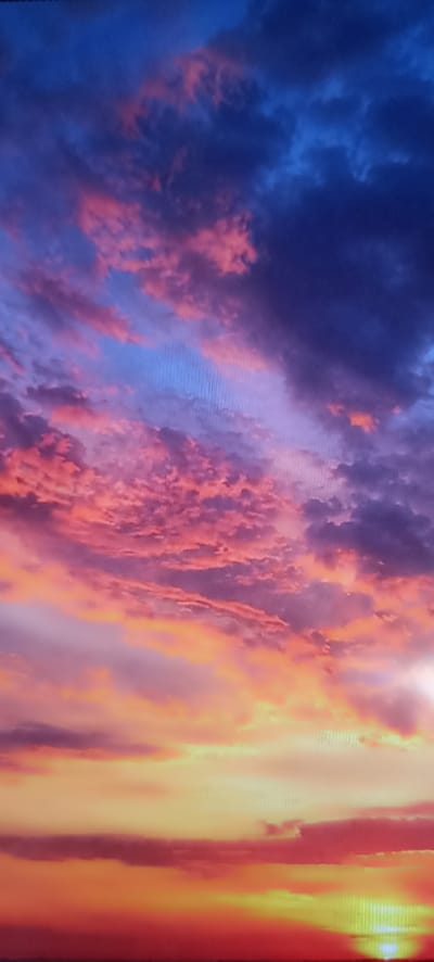 The image shows a dramatic sunset with vibrant colors. The sky is filled with clouds tinged with shades of pink, orange, yellow, and deep blue. The clouds are textured and appear to be moving, creating a sense of depth and motion. The lighting suggests that the sun is low on the horizon, casting a warm glow across the scene. There are no people, subjects, objects, or actions visible in the image. The location is specified as Chekhov-2, Russia.