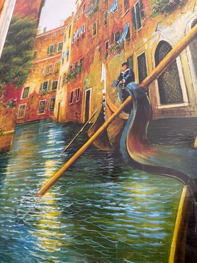 The image is a painting depicting a gondola in Venice, Italy. A gondolier stands in the stern, operating the boat. The gondola is moving through a canal, with buildings lining the waterway. The architectural style suggests Venice. The water reflects the buildings and the gondola. The painting style is impressionistic or painterly. The buildings are multi-storied with various windows and details, indicating an urban setting. The environment suggests a sunny day with reflections in the water. The painting captures a typical Venetian scene. The city of Azuqueca de Henares, Spain, is not visible in this image.