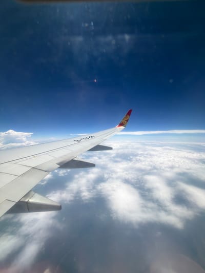The image, taken from an airplane window, depicts a view above a layer of clouds. The wing of the airplane is prominently in the foreground, with its serial number B-1928 visible. The tail fin of the aircraft, featuring a red and gold logo, is also visible. The sky above is a deep blue, indicating a high altitude. The clouds below appear dense and white, stretching across the horizon. While the image itself does not provide any specific landmarks or visual cues to pinpoint the location in Changzhi City, China, it captures a typical scene from an airplane in flight, likely over a vast expanse of clouds.