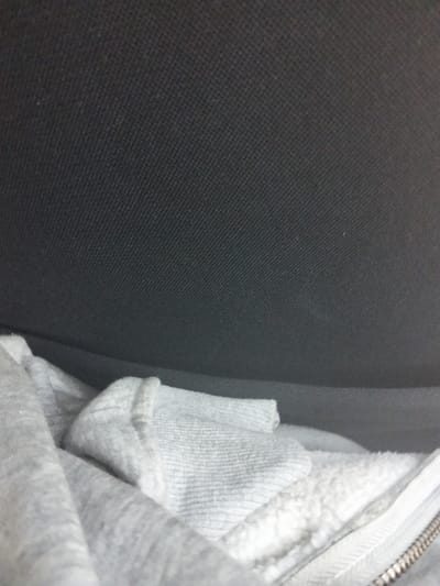 The image depicts an interior scene in Viwandani ward, Kenya. A light grey, heathered fabric garment, appearing to be a hooded sweatshirt or jacket, occupies the lower third of the frame. The garment exhibits a soft, fleece-like interior texture and a white plastic zipper with a metallic pull tab is partially visible on its right side. The upper two-thirds of the image features a dark grey or black textured fabric surface, likely upholstery, creating a background for the garment. The grey garment appears rumpled, positioned against or within the dark fabric structure. No individuals, specific actions, or direct interactions are visible.