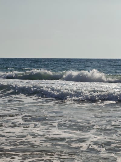 The image shows a body of water with waves. The water is a deep blue and the waves are white with foam. The sky is a pale gray and there is no sun visible. The scene is serene and peaceful. The image is not specific to Saiyn, Kazakhstan and provides no information about this location.