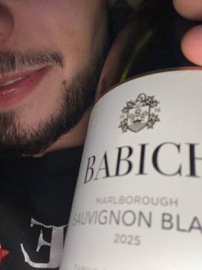A man is pictured holding a bottle of "BABICH MARLBOROUGH SAUVIGNON BLA" wine (2025) close to his face. The man has dark hair, stubble, and is wearing a black shirt or t-shirt. The city of Petarch, Bulgaria is not mentioned in the image or surrounding text.