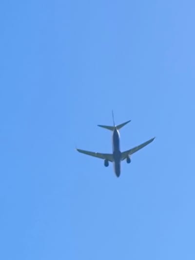 The image depicts a clear blue sky with an airplane flying overhead. The airplane is silhouetted against the sky, with its wings, fuselage, and tail visible. The perspective is from below, looking up at the aircraft. The scene appears to be outdoors, likely in an open area such as a field or park, but no specific urban elements or landmarks are visible to indicate its location within Vētras, Latvia. The focus is solely on the airplane and the sky.