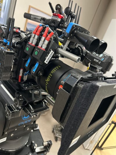 This image is a close-up shot of a professional film camera. The camera is equipped with various accessories including a lens with focus marks, a viewfinder with the letters "MVF-2", focus motors with red cables, and other specialized components. Text visible on the camera includes brand names "ARRI", "KONDOR BLUE", "NE", and the word "OVIDE". The camera appears to be indoors. There is no information available in the image that would indicate that this image was taken in Tres Cantos, Spain.