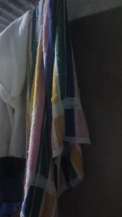 The image shows a stack of folded textiles with horizontal stripes in various colors, including blue, green, yellow, and pink. Some of the textiles also have a white pattern. The lower portion of the stack includes a larger white textile. The background is dark and out of focus, suggesting a low-light environment. The image does not contain information regarding the location of Putucual, Venezuela.