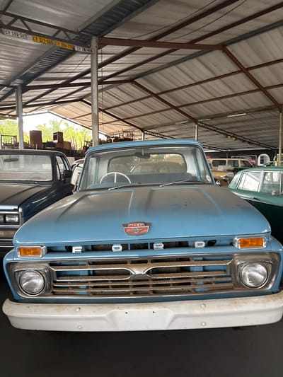 The image shows the front of a light blue Ford pickup truck parked inside a large warehouse or storage facility. The truck is positioned closely to other vehicles, with the front grille prominently visible. The environment appears to be a car storage or maintenance facility, possibly in a rural area, given the lack of surrounding urban features. While the exact location in Kraaifontein, South Africa cannot be determined from this image alone, the general environment seems indicative of a storage/workshop area.