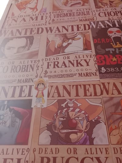 The image displays a collage of WANTED posters, likely from the anime/manga series One Piece, layered on a wall. The posters feature characters with their names and bounties. Prominently visible are posters for Nami, Vinsmoke Sanji, Chopper, Nico Robin, Franky, and other characters. The posters are in varying states of visibility, with some overlapping others. A small drawing of Monkey D. Luffy is placed near the center. The overall impression is of a decorative wall display rather than an actual crime scene. There is no indication of the city of San Marcos, El Salvador, or any forensic details related to a crime.