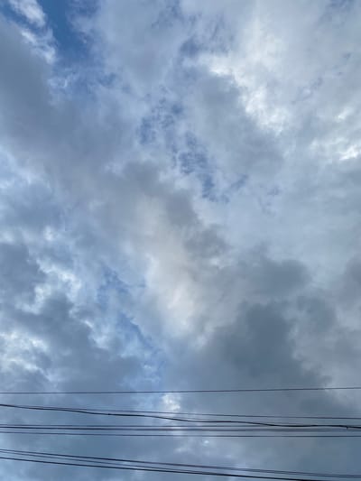The image shows a cloudy sky with several power lines running horizontally across the lower portion of the frame. The sky is filled with a mix of light and dark grey clouds, with patches of blue sky visible through the thinner clouds. There are no people or specific structures visible that would indicate a location in Murdash, Kyrgyzstan. The scene is a generic depiction of an outdoor environment with overhead electrical infrastructure against a cloudy sky.