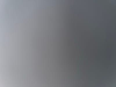 The image displays a smooth, abstract gradient of gray tones. The bottom left portion of the image is a very light gray, almost white, which gradually transitions to a darker, medium-to-dark gray towards the top right corner. The change in color is continuous and subtle, with no harsh lines or discernible patterns. There are no specific objects, people, scenes, or activities depicted. No text is visible in the image. The overall impression is one of a uniform, untextured surface transitioning in shade, potentially suggesting a lighting effect or a simple background.