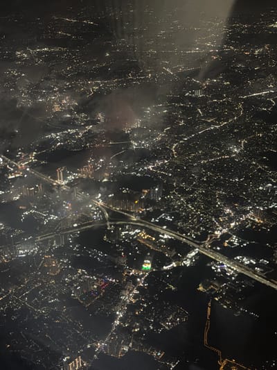 This is an aerial, night-time photograph of a densely populated urban area. The image is dominated by the glow of city lights, indicating a significant population and infrastructure. The lights are a mixture of white, yellow, and occasional red and blue hues, suggesting various types of lighting, from streetlights and buildings to possibly decorative or signage illumination.

The scene appears to be a sprawling cityscape with a network of roads and highways visible as brighter lines cutting through the darker areas. There are numerous clusters of buildings, many of which are tall and appear to be high-rise apartments or commercial structures, evidenced by the vertical lines of light. In some areas, the lighting suggests a more diffuse residential pattern. There are also darker patches, possibly indicating bodies of water, parks, or unlit areas.

The photograph captures the characteristic illumination pattern of a major city at night, where human activity is concentrated and visible from above. The presence of multiple levels of infrastructure, from major arterial roads to smaller, intricate lighting patterns, suggests a complex and active urban environment.

Specifically, identifying the location as Narsingi, India, implies that this image is capturing a part of the Hyderabad metropolitan area. Narsingi is known for its rapid development, including residential complexes and commercial hubs. The aerial view would likely show the concentration of these developments, characterized by the illuminated high-rise buildings and the extensive road networks connecting them, all typical of a rapidly growing urban periphery in India. The scale and density of lights are consistent with a significant urban center. There are no discernible individuals or specific actions captured in this high-altitude, night-time overview. The environment is entirely artificial light in a man-made landscape.