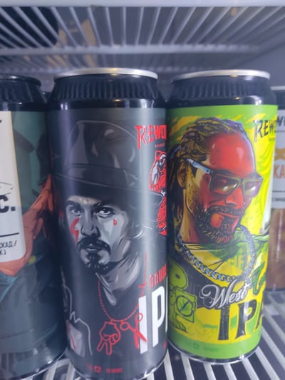 The image shows three cans of beer stacked on top of each other, presumably in a refrigerator in a store or bar.

The top can has a bright yellow-green label with a cartoonish depiction of a man with red skin, wearing sunglasses, and smoking a cigarette. A gold chain is draped around his neck. The words "West IP" are prominently displayed on the can. The brand Rewort is identified on the beer can.

The middle can has a dark grey label with a stylized drawing of a person with facial markings, wearing a hat. Red graphics, including scissors and a hand gesture, are visible on the label. The Rewort beer brand is also present on this can.

The bottom can is partially visible and shows a green label. The cans appear to be in a retail setting, possibly in Pskov, Russia. The vertical metal bars of the refrigerator are visible in the background.