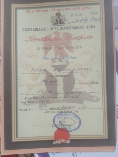 The image displays a framed certificate from the Government of Imo State, Nigeria. The certificate is for the ABOH-MBAISE LOCAL GOVERNMENT AREA and is an Identification Certificate. Text on the certificate indicates it is to whom it may concern and certifies that Hilary Ezindu Hilary is an indigene of Akuwa, Uvurli, in Aboh Mbaise Local Government Area of Imo State of Nigeria. The certificate is dated the 2nd day of April, 2013. It includes a space for an authorized signature and a stamp for the DAGS/Secretary, Aboh Mbaise Local Government. The certificate features decorative elements, including what appears to be an eagle and a horse. The location of Magajin Gari, Nigeria is not mentioned or depicted in this image.