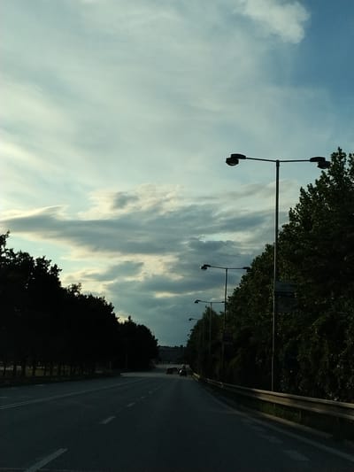 The image depicts a road with streetlights and trees lining one side. The sky is cloudy with patches of blue. There are a few cars on the road. The overall impression is of a highway or a major road on the outskirts of a city. The provided location of Malé Nepodřice, Czechia, suggests this is a scene from that area.