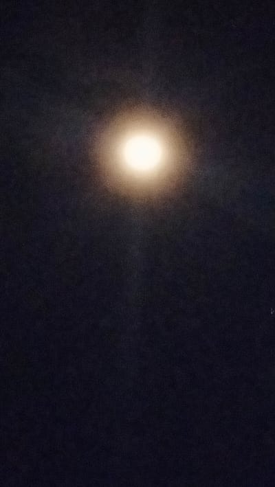 The image depicts a full moon in a dark sky. The moon is bright and appears to be the primary subject. The sky is a deep, dark hue, likely representing nighttime. There is a subtle glow or haze surrounding the moon, suggesting it might be partially obscured by thin clouds or atmospheric conditions. The overall impression is that of a clear night sky with a prominent celestial body. The image is taken vertically, with the moon positioned roughly in the upper center. No specific details of Barat Yaman, Indonesia are visible in this image, as it is a celestial scene.