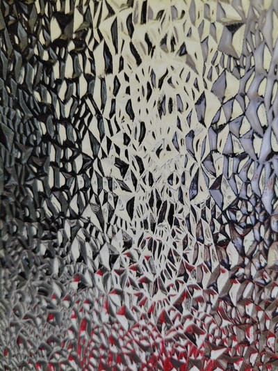 The image is a close-up, abstract photograph of a textured surface, possibly patterned glass or a similar material. The surface features an irregular, faceted pattern that distorts the light and reflections.
The subjects are purely visual elements created by the interaction of light with the textured surface. There are no discernible people, objects, or a specific scene. The setting is undefined, as the focus is entirely on the tactile and visual quality of the surface.
No activity or event is taking place. The image captures a static texture.
Notable details include the play of light and shadow, which creates a mosaic-like appearance with irregular shapes. Areas of bright white and light gray reflect light intensely, while darker areas appear to be in shadow or are deeper indentations in the texture. There are also hints of color, particularly patches of red and black, which are reflected or embedded within the texture, adding depth and contrast. The texture itself appears to be made up of many small, angular facets, giving it a somewhat crystalline or broken-glass appearance. There is no indication of the time of day, weather, or specific location beyond the general context of Petreni, Moldova, which is not visually evident in the photograph. No emotions are conveyed as there are no living subjects.
There is no visible text in the image.