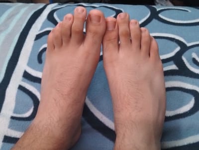 A close-up captures a pair of feet resting on a patterned blue and white surface. The skin tone is light, with fine hairs visible on the feet and ankles. The toes are neatly arranged, showing trimmed nails. The backdrop features alternating blue and white stripes and loop patterns. The scene exudes a casual, relaxed atmosphere.