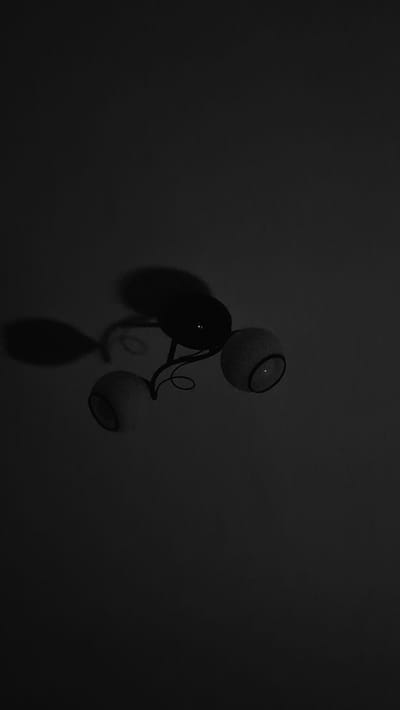 The image shows a black and white, low-light, and underexposed photograph of a ceiling light fixture. The fixture has a dark, ornate metal stem with a central bulb holder, from which two additional light shades extend. The shades are spherical and appear to be made of frosted glass or a similar material, with a dark rim around their openings. Shadows are cast on the ceiling from the fixture, creating an abstract and somewhat eerie atmosphere. The overall impression is of a dimly lit interior space, likely a room within a building.

Given the request for location information in Ialoveni, Moldova, it is important to state that the image itself provides no visual cues or context to place it specifically in that city. The scene is generic and could be found in any location with a similar interior design.