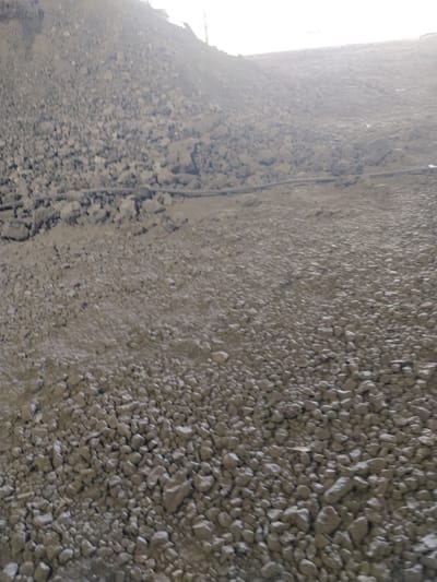 The image depicts a large, desolate landscape dominated by piles of grey, rocky debris. The terrain appears to be a construction site or an industrial area, with a significant incline in the background. A dark, horizontal line, possibly a pipe or cable, is visible traversing the middle ground of the scene. The sky overhead is bright and washed out, suggesting either daylight or artificial illumination. There are no people, animals, or vehicles visible in the frame. The overall impression is one of barrenness and industrial activity, possibly related to mining or large-scale earthmoving operations. The location is Dąbrowa Górnicza, Poland.