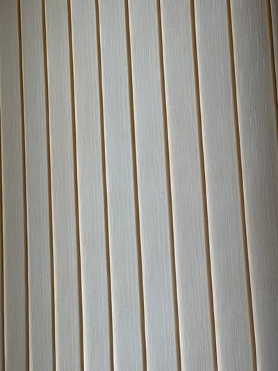 The image shows a close-up view of horizontal window blinds. The blinds are a light, neutral color with a subtle textured pattern. They are positioned at an angle, creating alternating bands of light and shadow. No people, subjects, or actions are depicted in the image. The location in Baiachevo, Bulgaria is not discernible from the image alone.