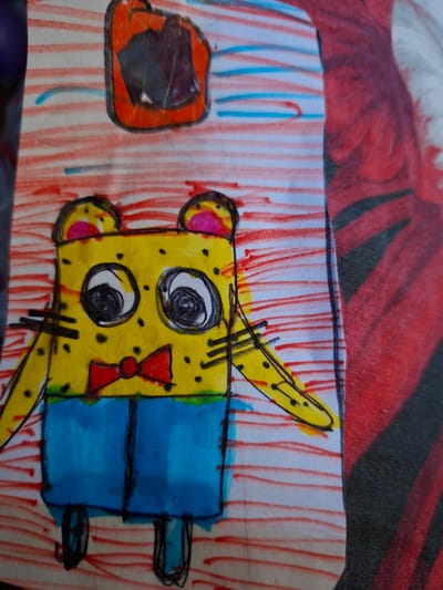 This media file features a close-up, overhead view of a child's drawing on white paper, with red and blue crayon lines forming a striped background. The central subject is a yellow, cartoonish creature, possibly a stylized animal, with black spots, large circular eyes with black pupils, and round ears with pink centers. It wears a red bow tie. The creature has a blue rectangular body attached to its head. To the left of the creature is an orange, roughly square shape with a dark, irregular interior, also outlined in black. The drawing style is simplistic and childlike, with bold colors and uneven lines. The overall mood of the drawing appears whimsical and cheerful. The drawing is placed on top of a red and black patterned fabric, likely a piece of clothing or a blanket, which is also visible in the background and adds a textural element to the image. There is no visible text in the image. The location context of Pervouralsk, Russia, does not offer any specific visual cues within the drawing itself.