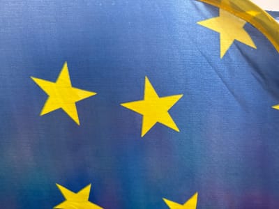 The image displays a close-up of a blue flag with yellow stars. The texture of the fabric is visible, suggesting it is a flag. A yellow border is partially visible at the top of the image, wrapping around the flag. The flag's design is consistent with the flag of the European Union. The image does not provide any context or details about its location in Brasília, Brazil, or any other environment. There are no people, actions, or interactions depicted.