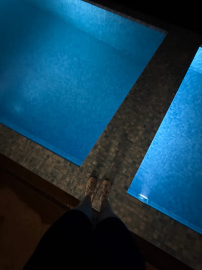 An overhead shot depicts two pools filled with blue water, separated by a tiled walkway. A person stands on the tiled walkway, wearing shoes and dark clothing. The photograph was taken indoors. Location: Jinhua, China.