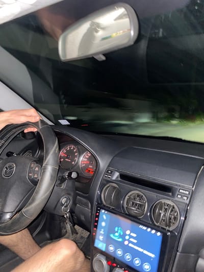 The image shows the interior of a car, looking forward through the windshield at night. The driver's hand is on the steering wheel, and the dashboard is visible with instruments like the speedometer and tachometer. A digital display is also present in the center console. The scene is dark outside the car, with streetlights or headlights illuminating a road. There is no visible indication of the specific location within the city of Yasen, Bulgaria.